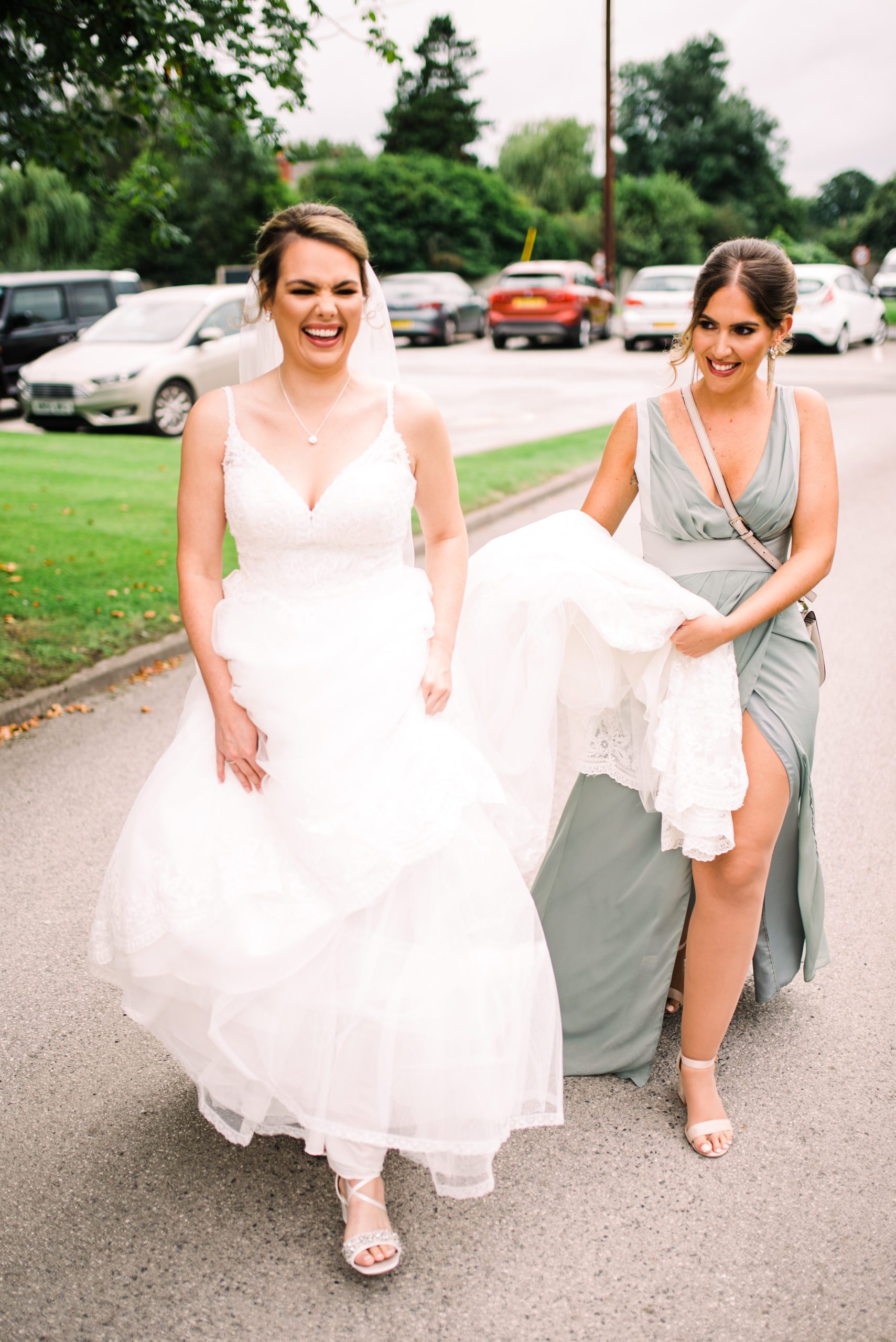 Bride walks and laughs as bridesmaid carries her train behind her