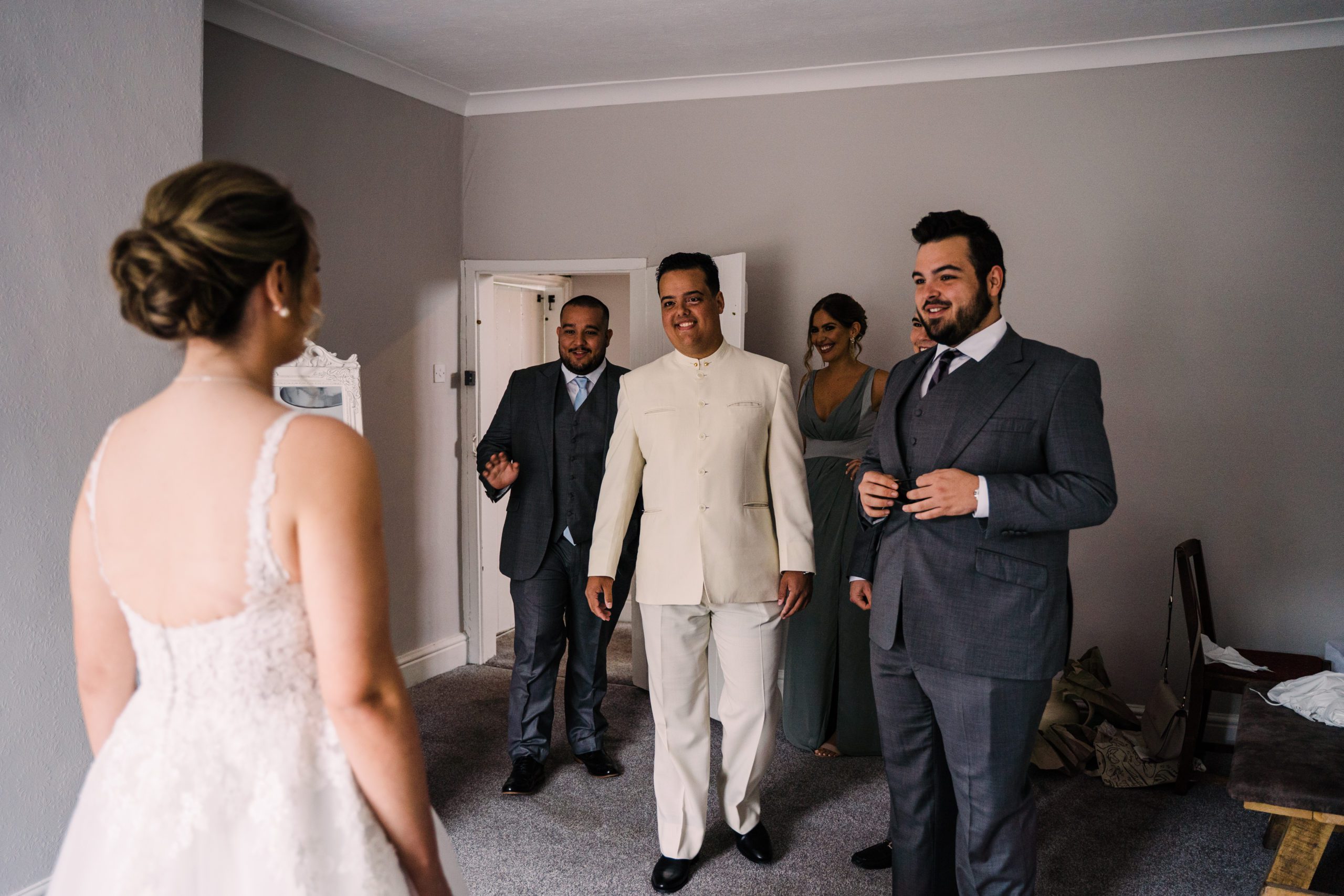 Bride has back to camera as brothers enter room smiling for first look.