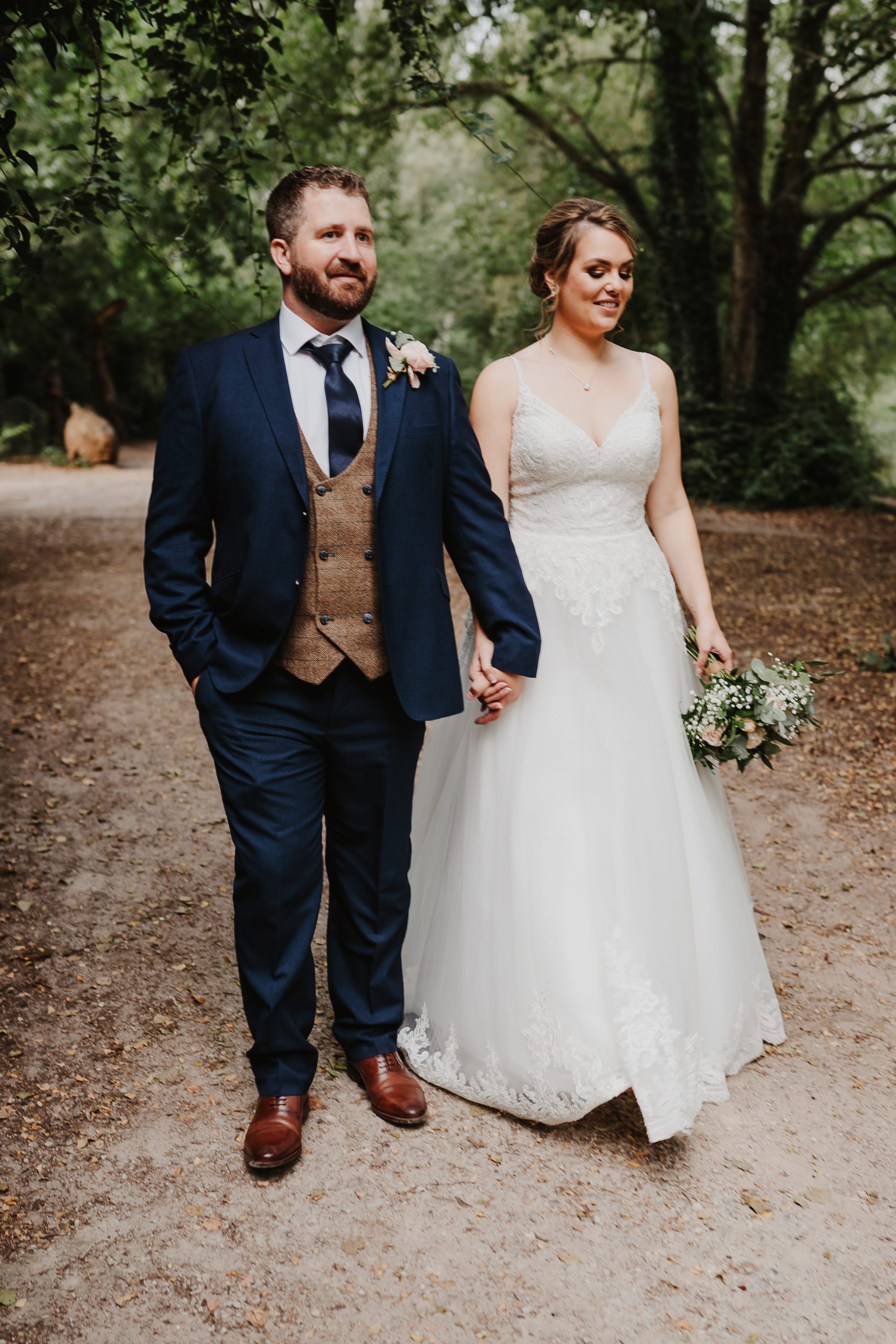 Full length shot of bride and groom holding hands and walking through woodland at Shakerley Mere.