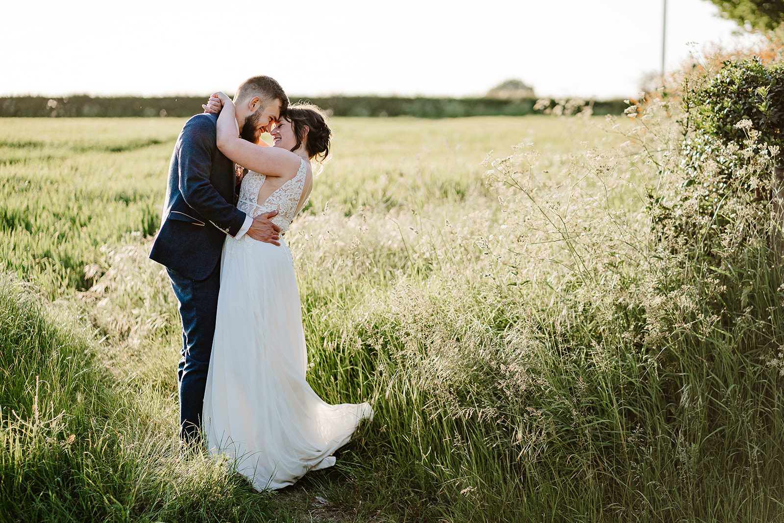 A bride and groom embrace in a sunlit field near Larkspur Lodge Wedding Venue in Knutsford