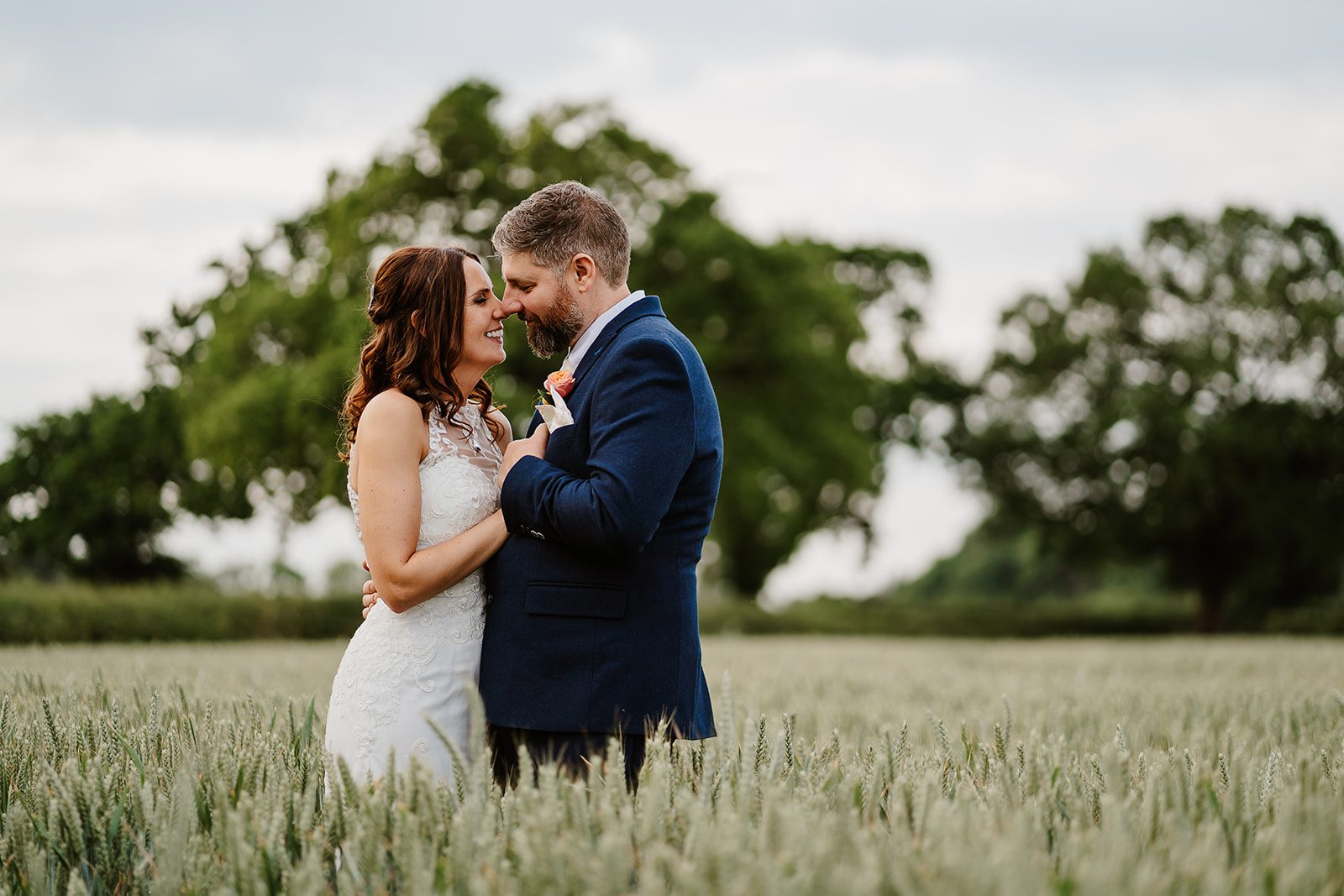 Bride and groom share an embrace nose to nose in wheat field at Stock Farm Barn Wedding Venue.