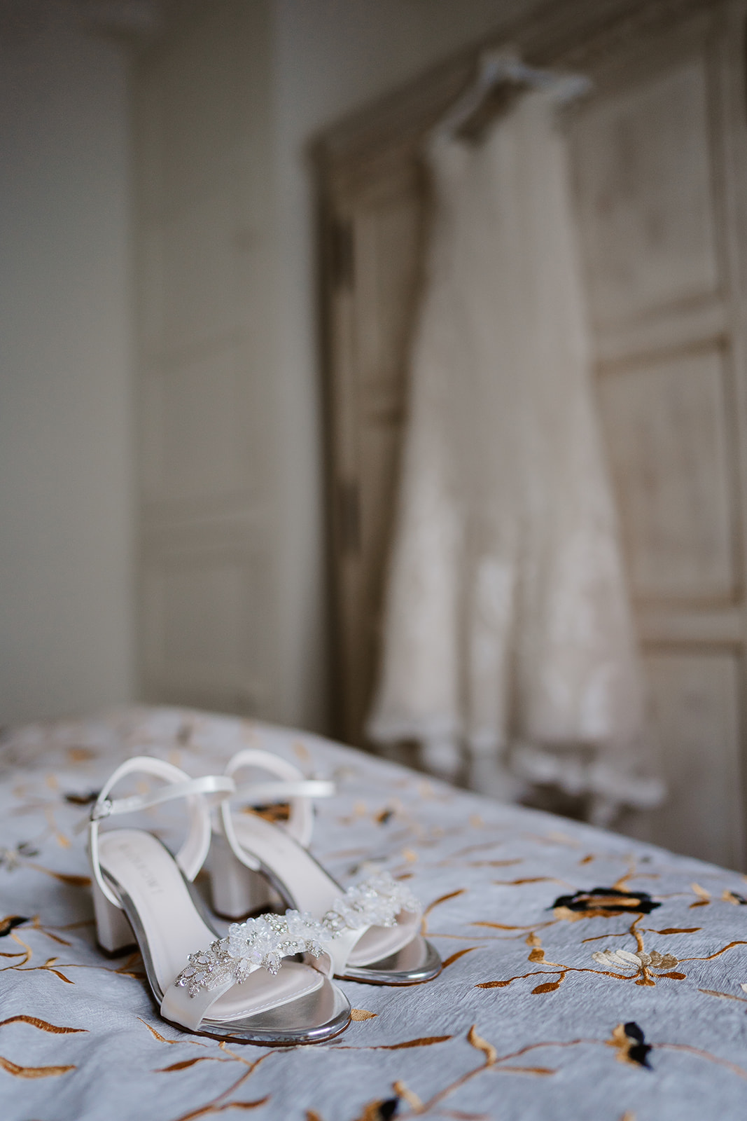 Wedding shoes on bed with dress hung in background
