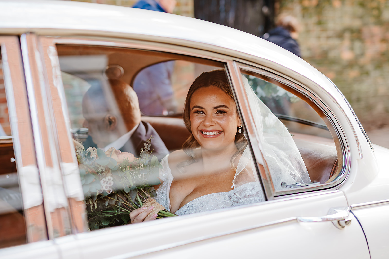 Bride smiling through window of white wedding car on arrival