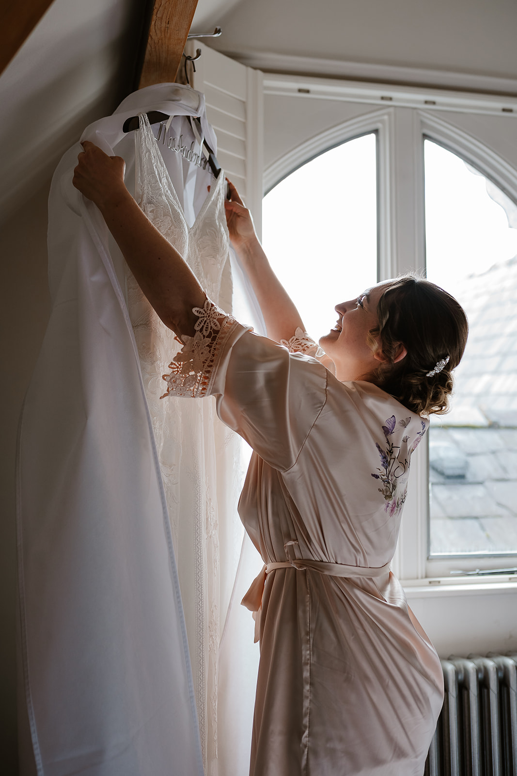 Bride unwrapping dress on hanger by window