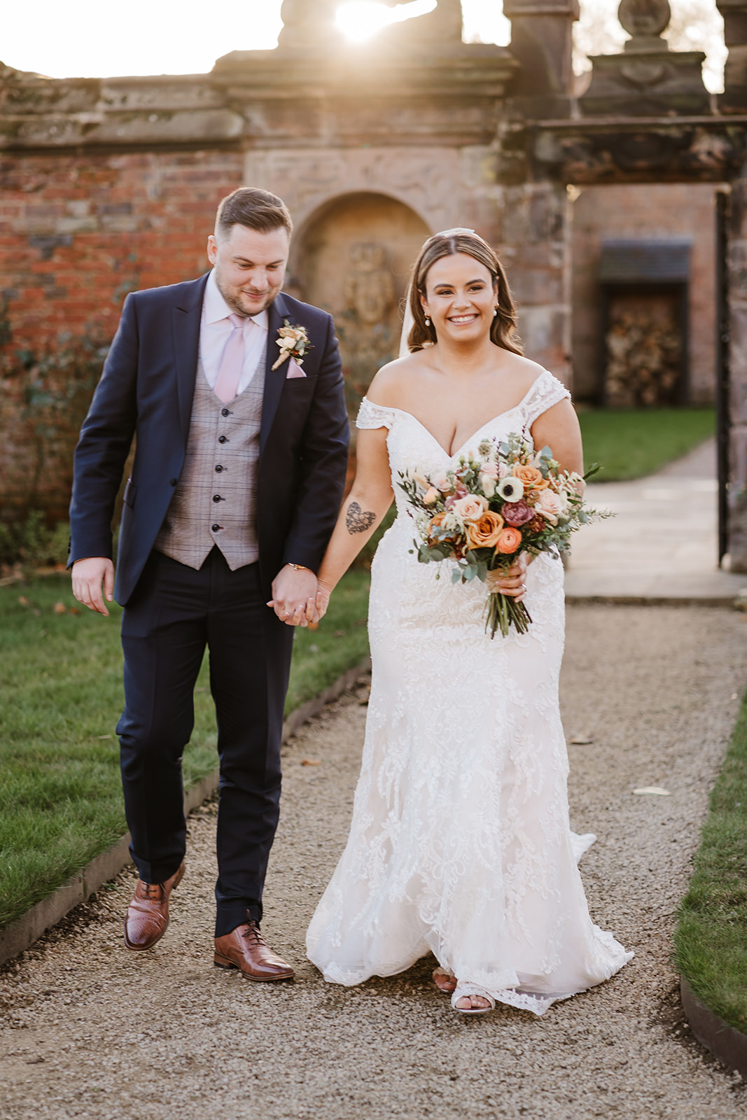 Bride and groom walk through stately home gardens in evening light
