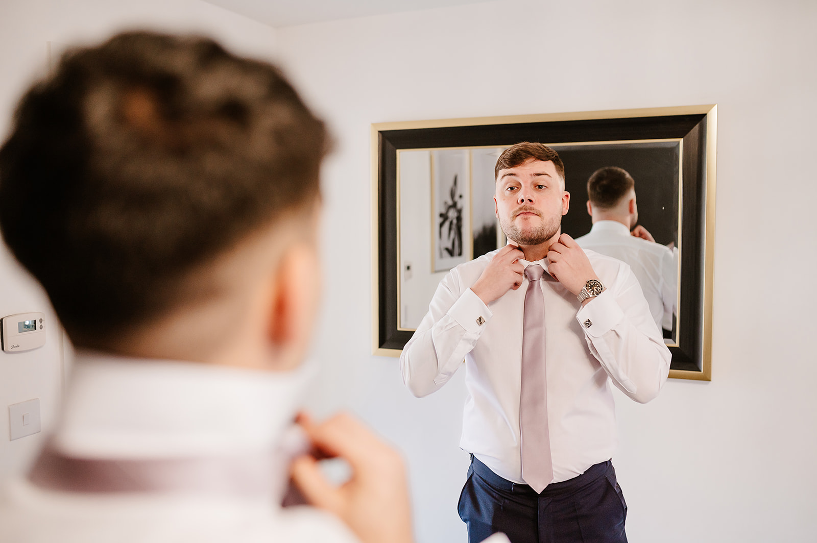 Groom adjusting collar in front of mirror