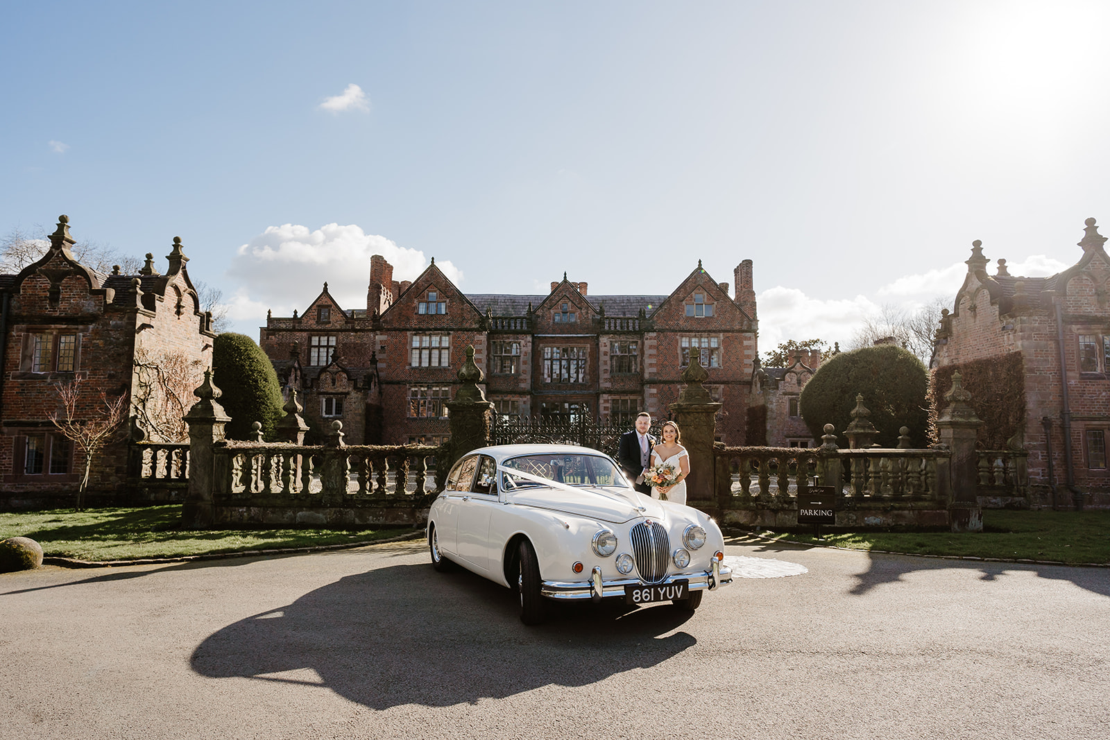 Bride and groom pose by car in front of Dorfold Hall