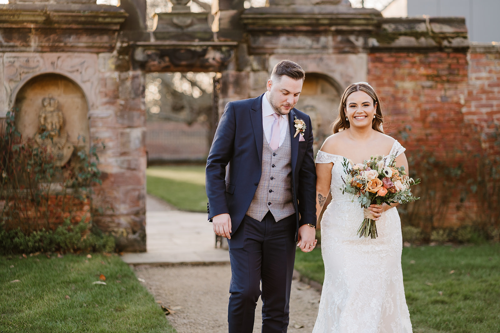 Bride and groom holding hands in stately home gardens