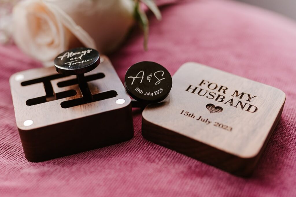 Close up photo of engraved cufflinks and a dark brown wooden laser engraved presentation box.  The inscription reads 'For My Husband'.  The box sits on top of a cerise coloured cloth. 